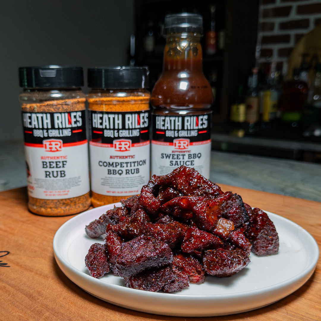 Heath Riles BBQ products including beef rub, competition BBQ rub, and sweet BBQ sauce with smoked meat on a plate.